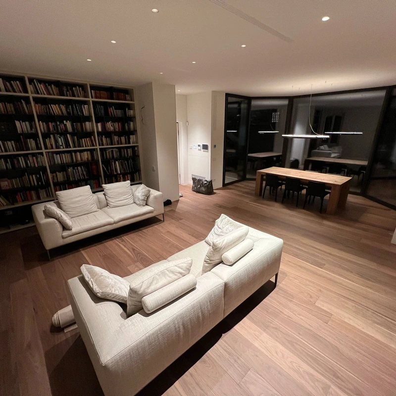 Salotto con libreria, divani chiari e pavimento in legno
